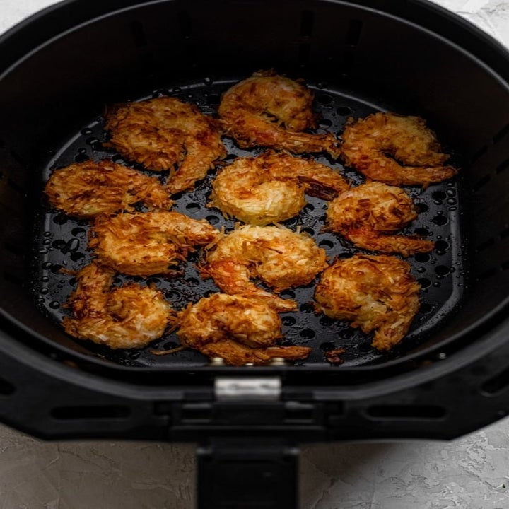 Several coconut shrimp getting crispy and browned in the air fryer.